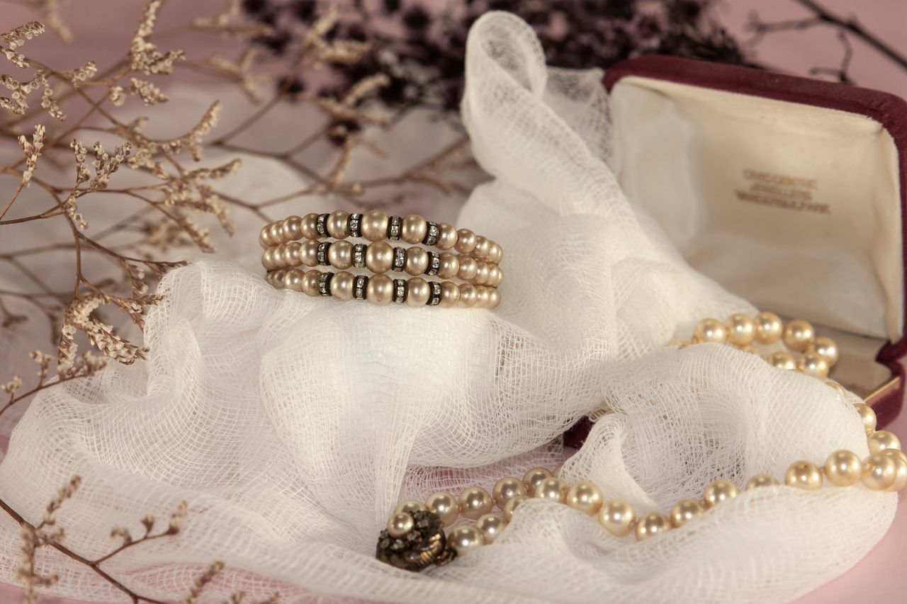 Close-up of pearl jewelry arranged on soft white fabric, with dried flowers.